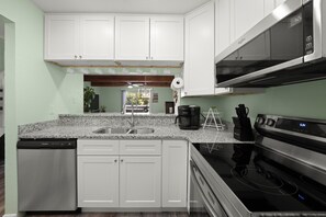 A kitchen with white cabinets, a stainless steel dishwasher, a black coffee maker, and a microwave. - Lakefront Luxury Retreat | Dock, Kayak & Views (Crossville)