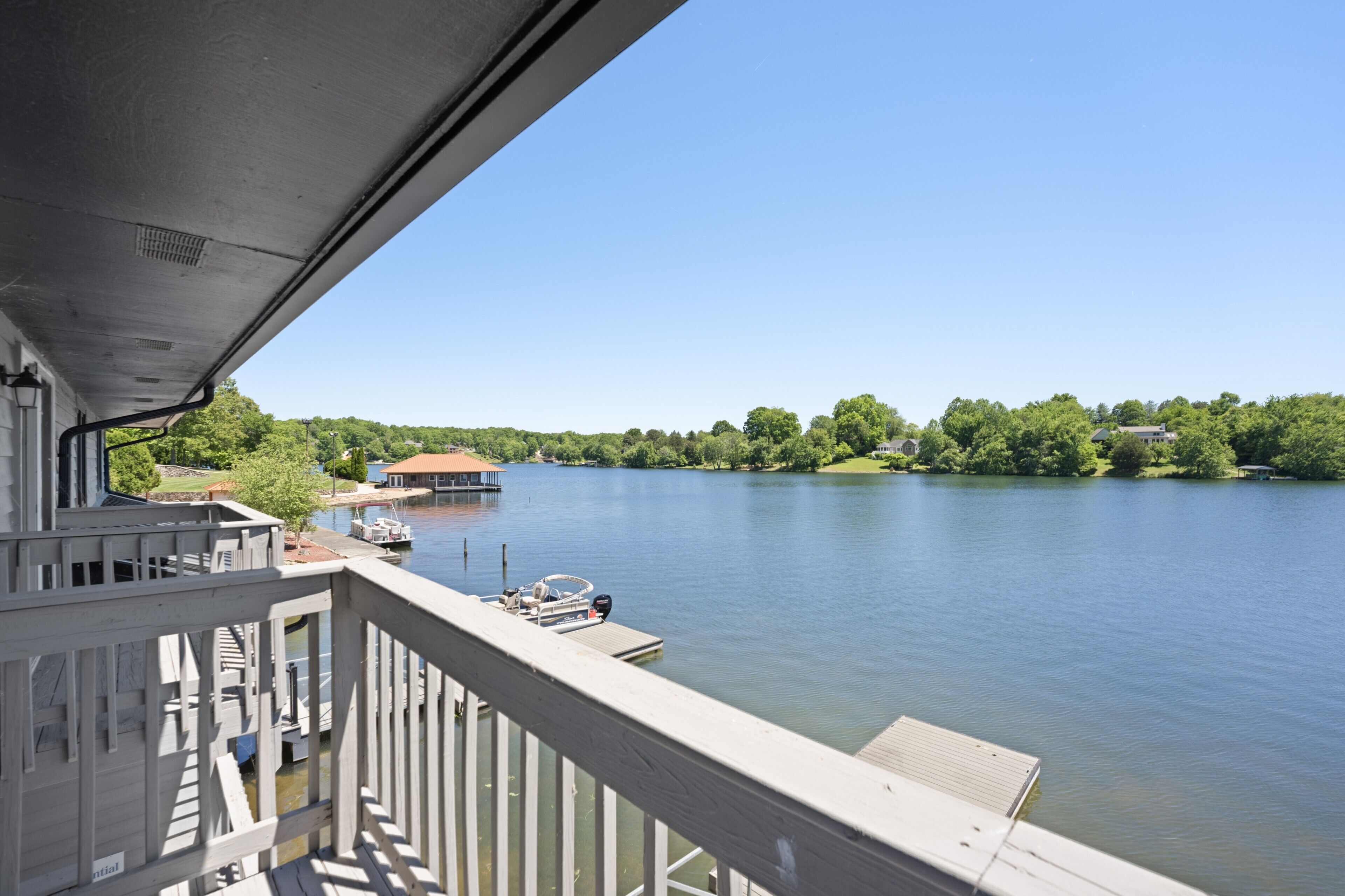 A lake with a dock and a boat, surrounded by greenery and a clear sky.