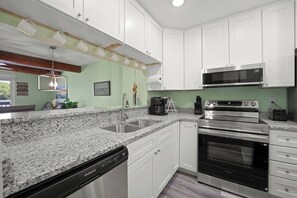 Eine Küche mit weißen Schränken, Granit-Arbeitsplatten, einem Edelstahl-Geschirrspüler, einer Mikrowelle und einem Backofen.