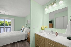 A bedroom with a bed, a nightstand, a dresser, a bathroom with a sink, mirror, and towel. - Lakefront Luxury Retreat | Dock, Kayak & Views (Crossville)