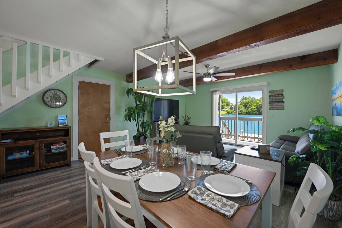A dining area with a wooden table set for four, a staircase, and a view of the outdoors.