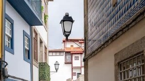 Una calle estrecha flanqueada por edificios, una farola y algunas mesas y sillas a lo lejos.