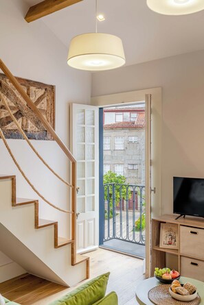 A modern interior with a staircase, a dining area with a bowl of fruit, and a television on a wooden cabinet.