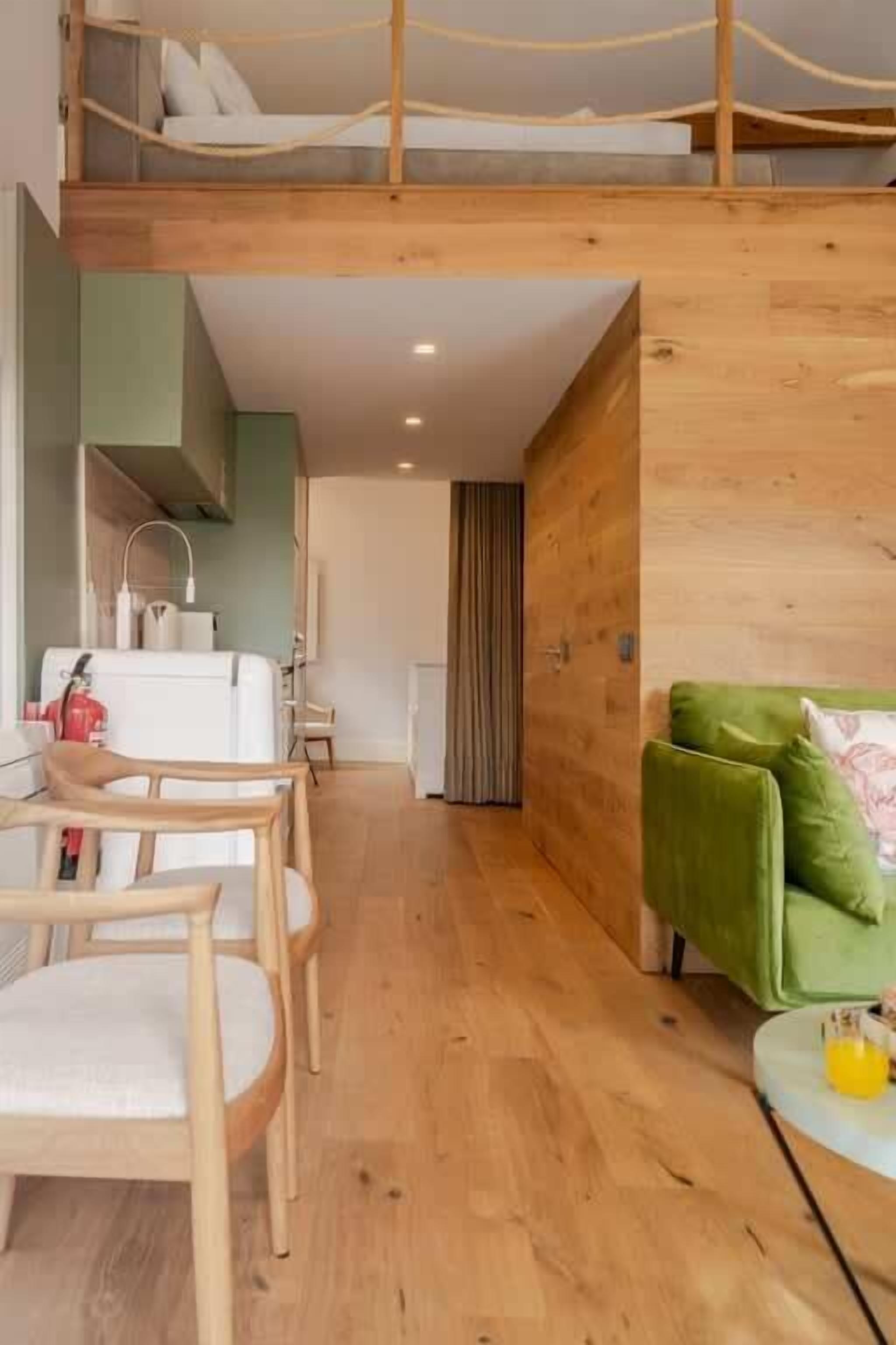A modern interior with a bunk bed, wooden flooring, a dining area with chairs, a green sofa, and a small table with a glass.