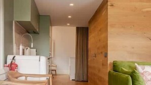 Un interior moderno con una litera, suelo de madera, una zona de comedor con sillas, un sofá verde y una pequeña mesa con un vaso.