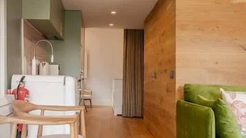 A modern interior with a bunk bed, wooden flooring, a dining area with chairs, a green sofa, and a small table with a glass.