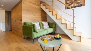 Un salón moderno con una escalera de madera, un sofá verde y una mesa redonda con frutas y una bebida.
