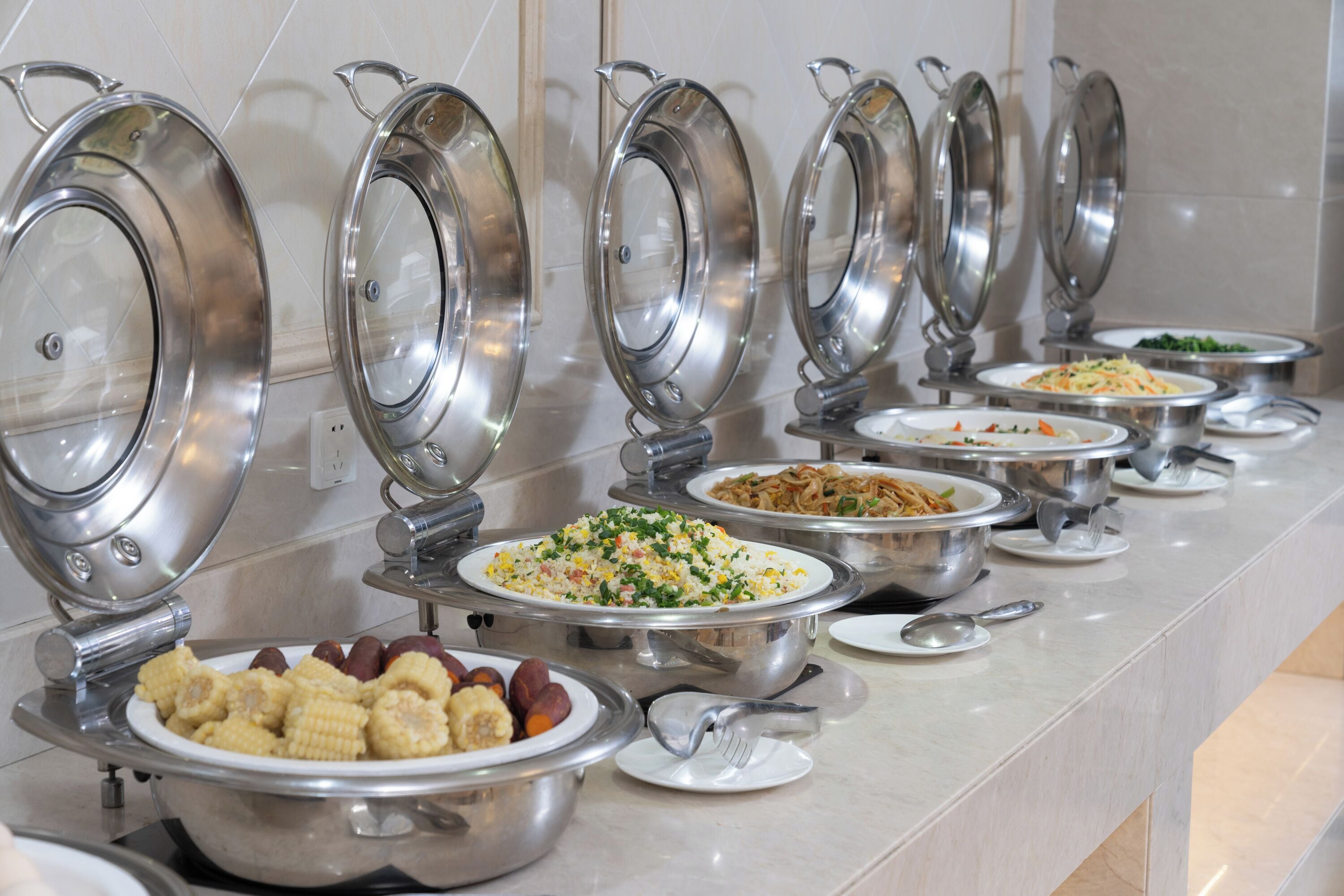 A buffet line with various dishes, including corn, rice, and vegetables, in a hotel setting.