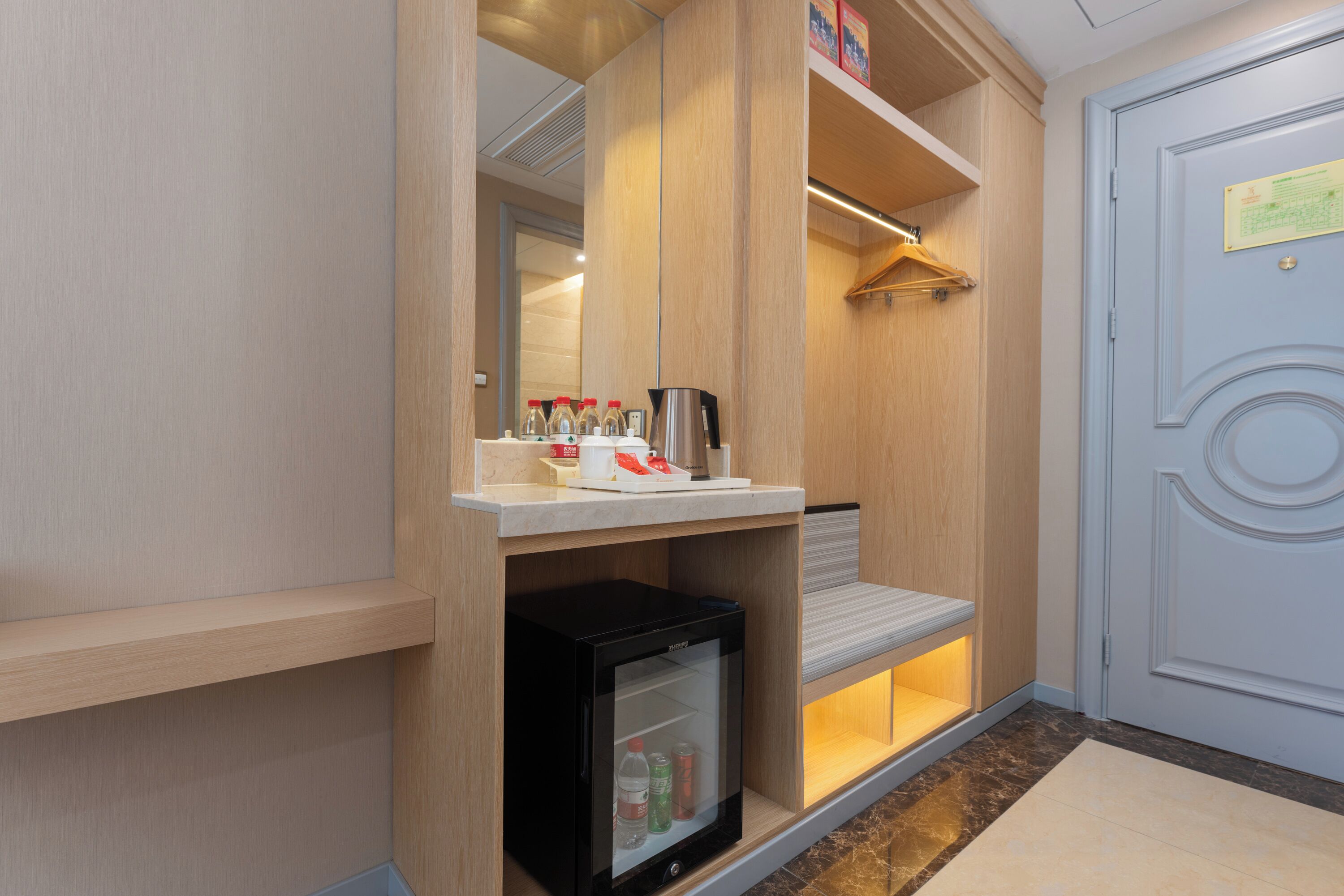 A hotel room with a minibar, a refrigerator, a coat rack, and a door with a sign.