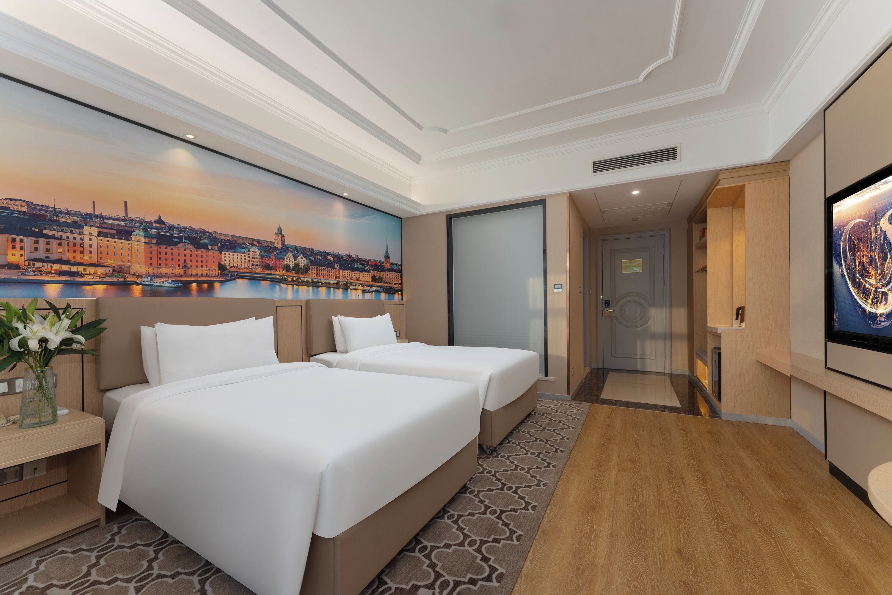 A hotel room with two beds, a large cityscape painting on the wall, a TV, and a wooden floor.