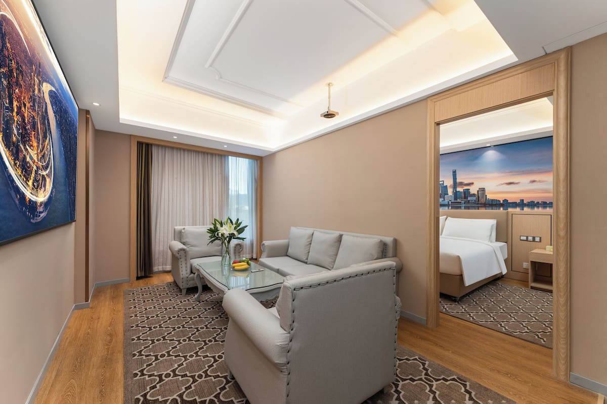 A hotel room with a sofa, a glass coffee table, a bed, a mirror, and a cityscape view.