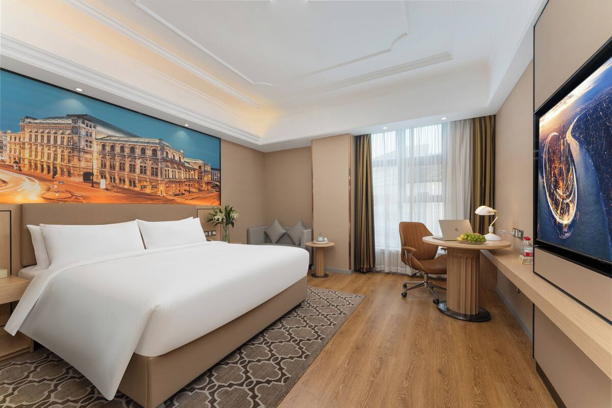 A hotel room with a large bed, a desk with a laptop, a chair, and a TV.