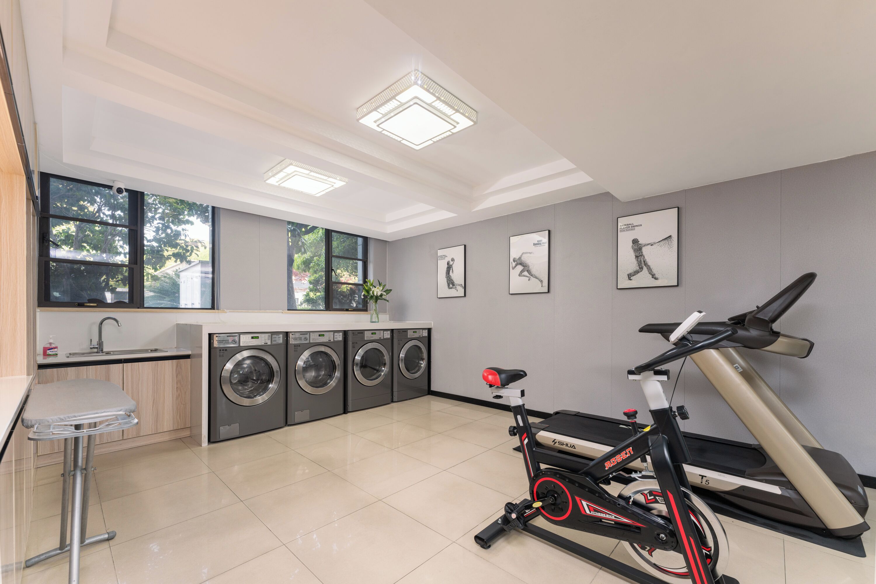 A modern laundry room with a large window, a washing machine, a dryer, and a stationary bike.