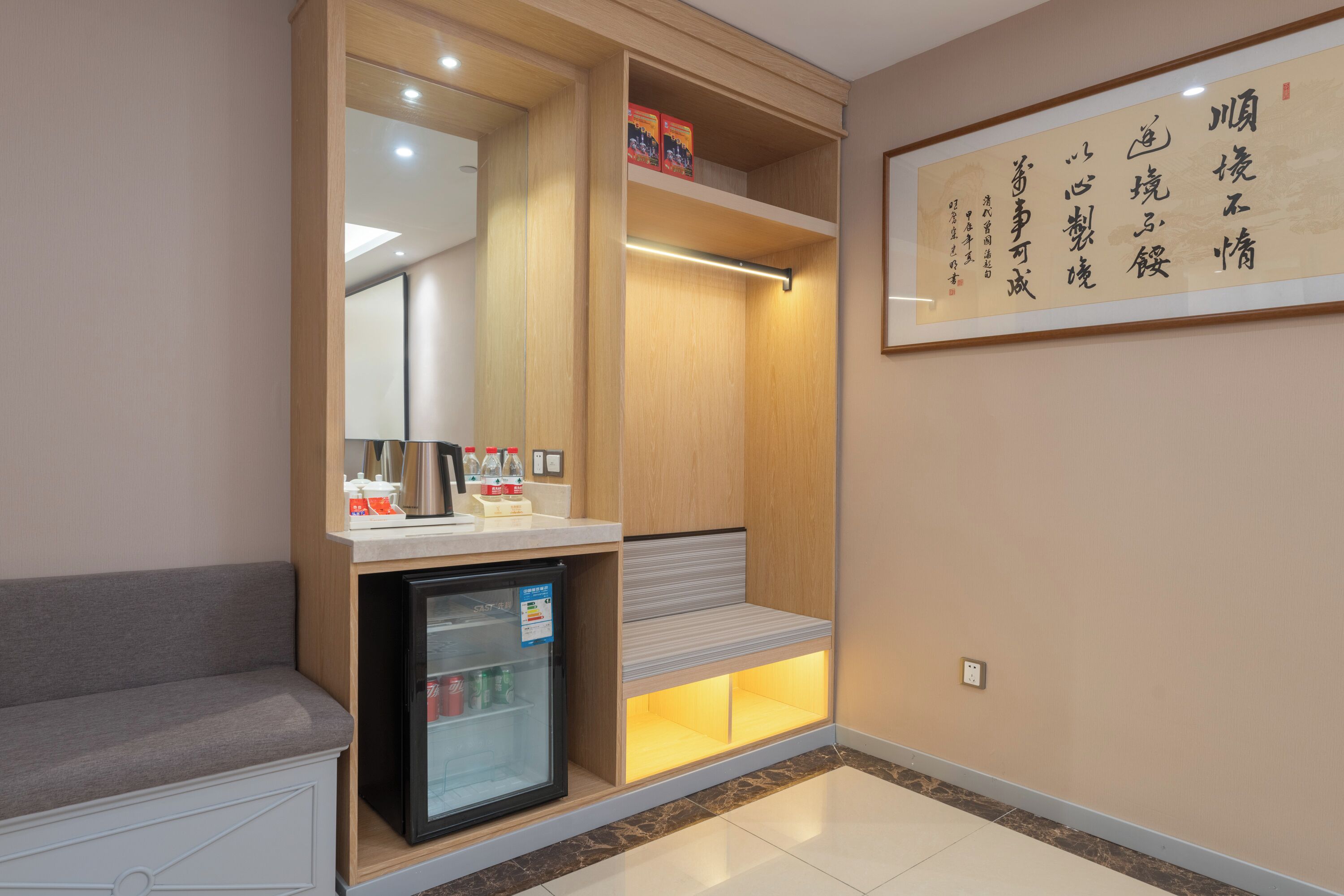 A hotel room with a minibar, a refrigerator, a seating area, and a wall with calligraphy.