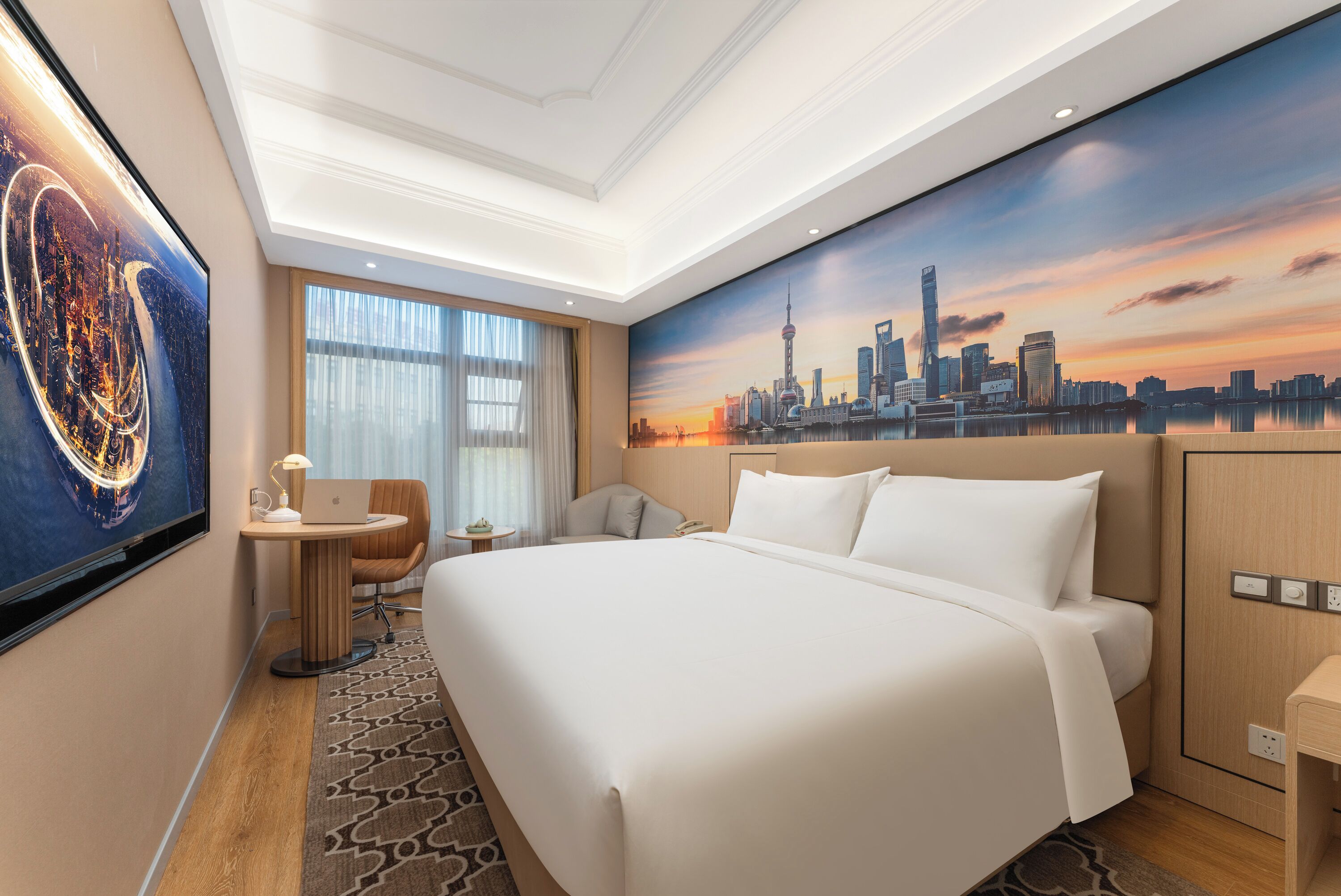 Habitación de hotel con una cama grande, un escritorio con una computadora portátil, una silla y un mural con vista a la ciudad en la pared.