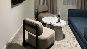 A modern living room with a sofa, armchair, and coffee table. A flat-screen TV is mounted on the wall, and a radiator is visible. - Nomad Camp (Kaji-Say)
