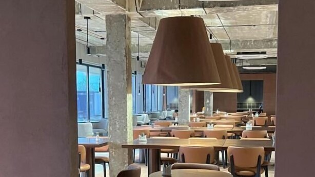 A modern dining area with round tables and chairs, large pendant lights, and a view into a spacious room with multiple tables and chairs. - Nomad Camp (Kaji-Say)