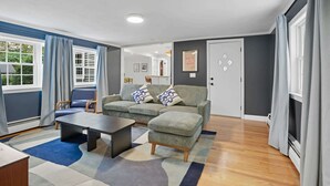 Ein modernes Wohnzimmer mit Sofa, Hocker und Couchtisch, einem Essbereich und Blick ins Freie.
