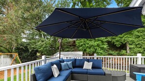 Eine Terrasse mit einer Eckcouch, einem Tisch, Stühlen und einem großen Sonnenschirm.