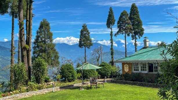 A lodge with a green roof, surrounded by tall trees and a mountain backdrop. - YuleTea Retreat A Premium Heritage Hotel (Darjeeling)
