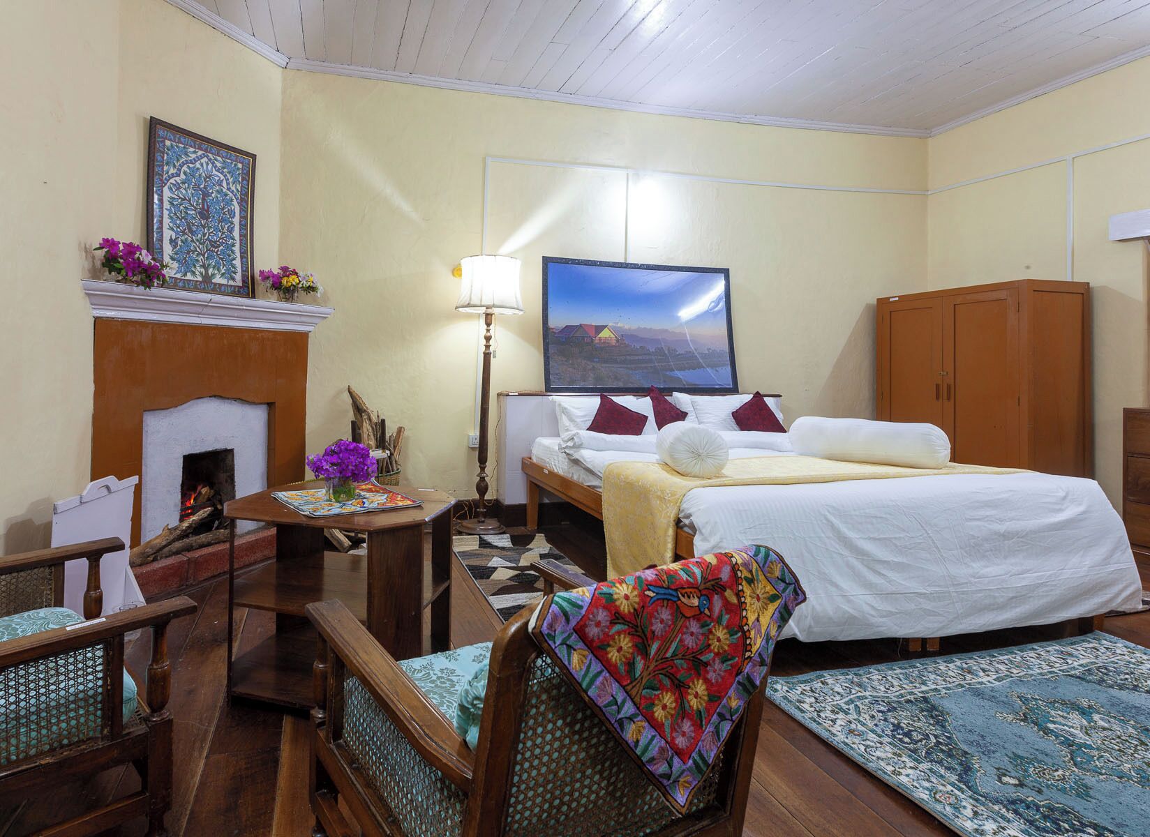 Een hotelkamer met een bed, een bureau, een stoel, een open haard, een schilderij en een kledingkast.