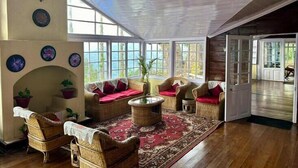 A spacious room with a high ceiling, large windows, wicker furniture, and a red patterned rug. - YuleTea Retreat A Premium Heritage Hotel (Darjeeling)