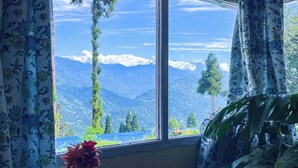 A room with a large window, a laptop on a table, and a vase with flowers. - YuleTea Retreat A Premium Heritage Hotel (Darjeeling)