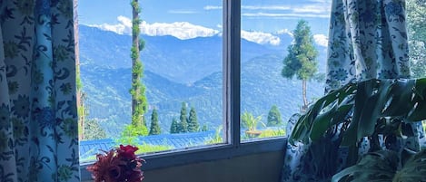 A room with a large window, a laptop on a table, and a vase with flowers.