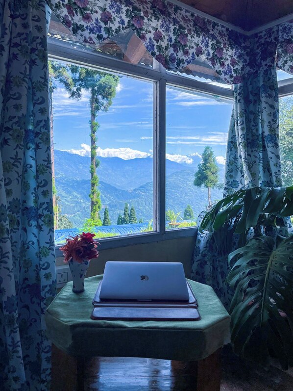 A room with a large window, a laptop on a table, and a vase with flowers.