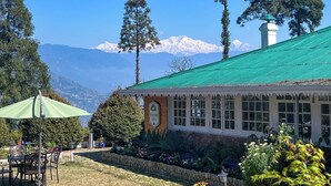 A building with a green roof, a clock, and a garden with a stone wall. - YuleTea Retreat A Premium Heritage Hotel (Darjeeling)