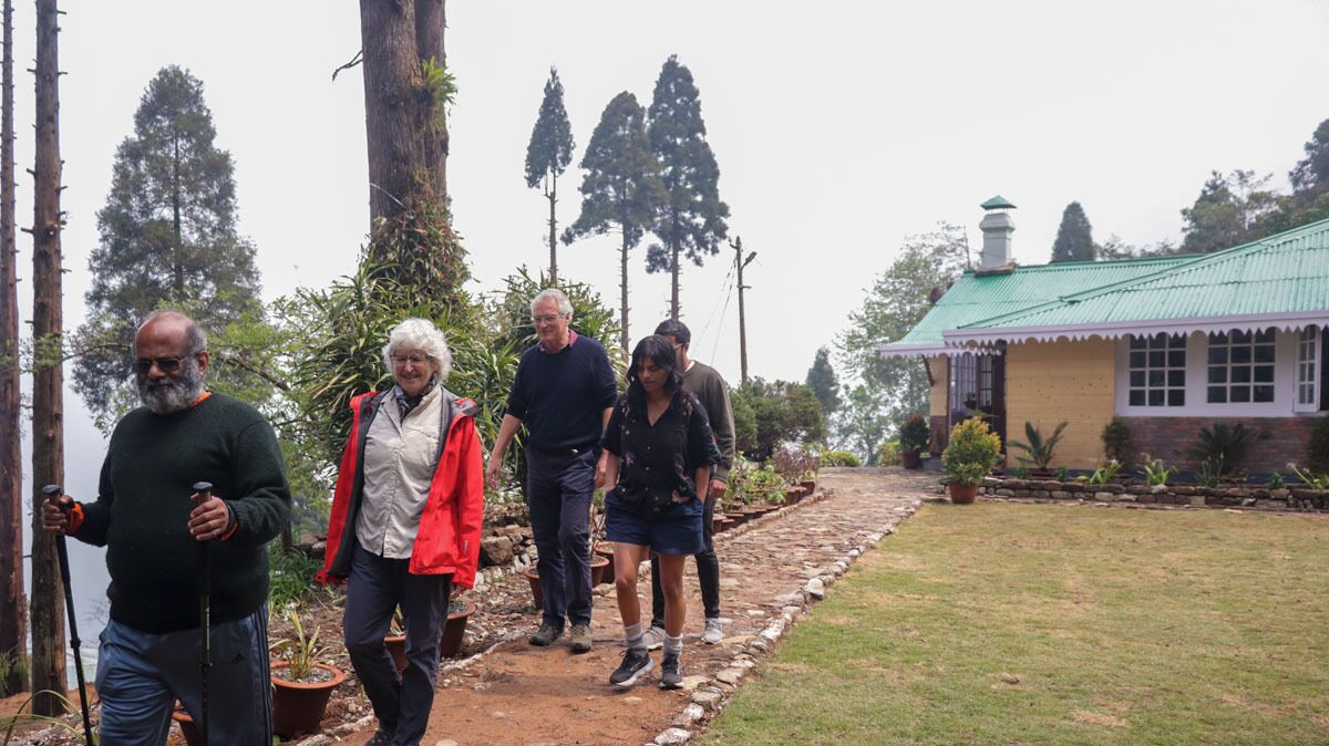 A group of people walking on a dirt path with a house in the background.