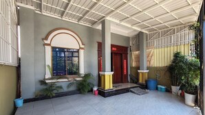 A covered outdoor area with tiled flooring, a window with a metal gate, potted plants, and a red door with Chinese characters. - TCN Condo 168 (Phnom Penh)