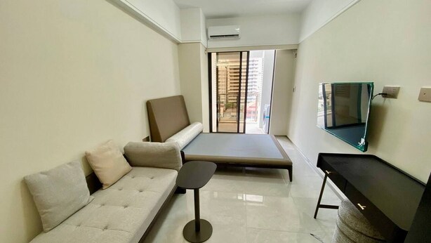 A compact living space with a sofa, a small table, a bench, and a TV on the wall. - TCN Condo 168 (Phnom Penh)