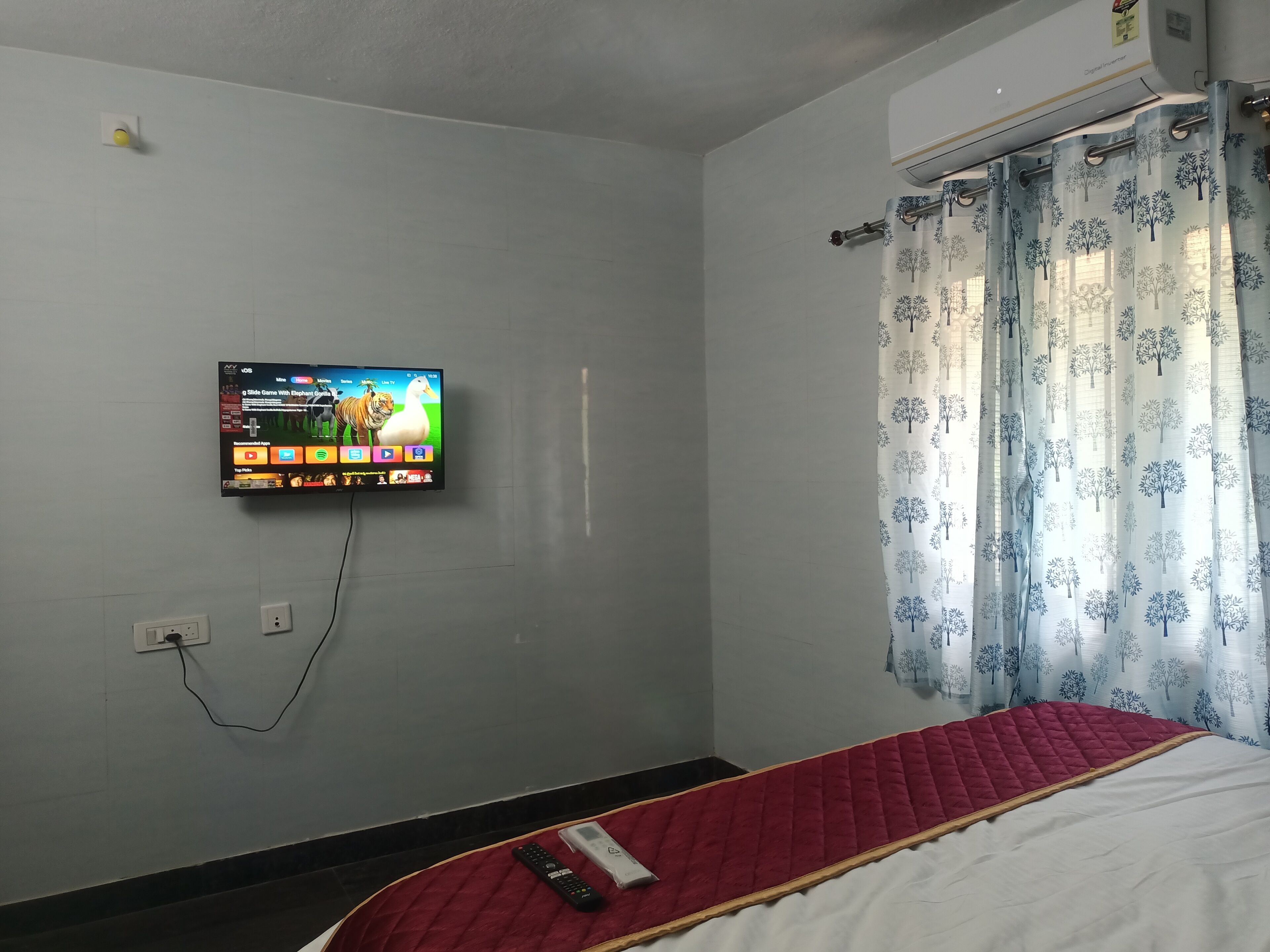 A room with a bed, a TV mounted on the wall, and a window with curtains.