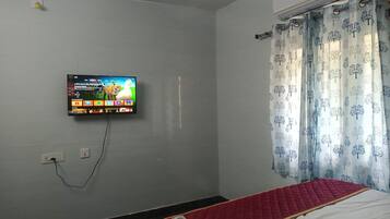 A room with a bed, a TV mounted on the wall, and a window with curtains.