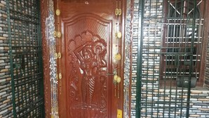 Een houten deur met gedetailleerde houtsnijwerken en een klassiek ontwerp, omlijst door stenen muren en metalen tralies.