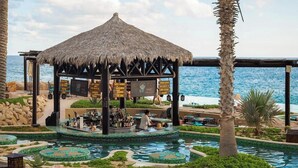 Eine Bar mit Strohdach, Pool und Palmen.