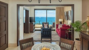 Ein geräumiges Wohnzimmer mit großem Fenster zum Meer, einer Kristallleuchter, einem roten Sofa und einem Essbereich mit Tisch und Stühlen.
