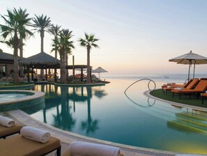 A resort pool with lounge chairs and umbrellas, surrounded by palm trees and a view of the ocean. -  Get away to the Grand Solmar Land's End Resort in beautiful Cabo San Lucas! (Cabo San Lucas)