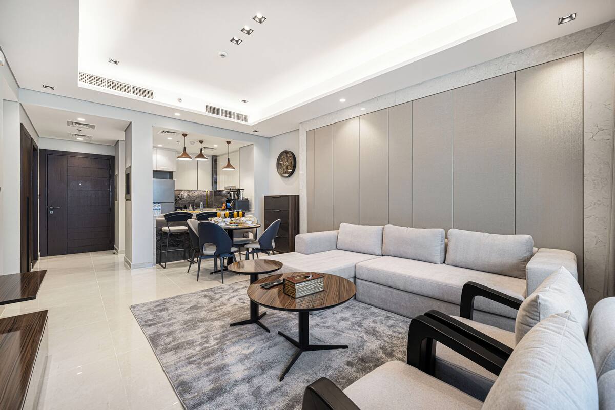 A modern living room with a sectional sofa, a coffee table, and a dining area with chairs and a kitchen in the background.