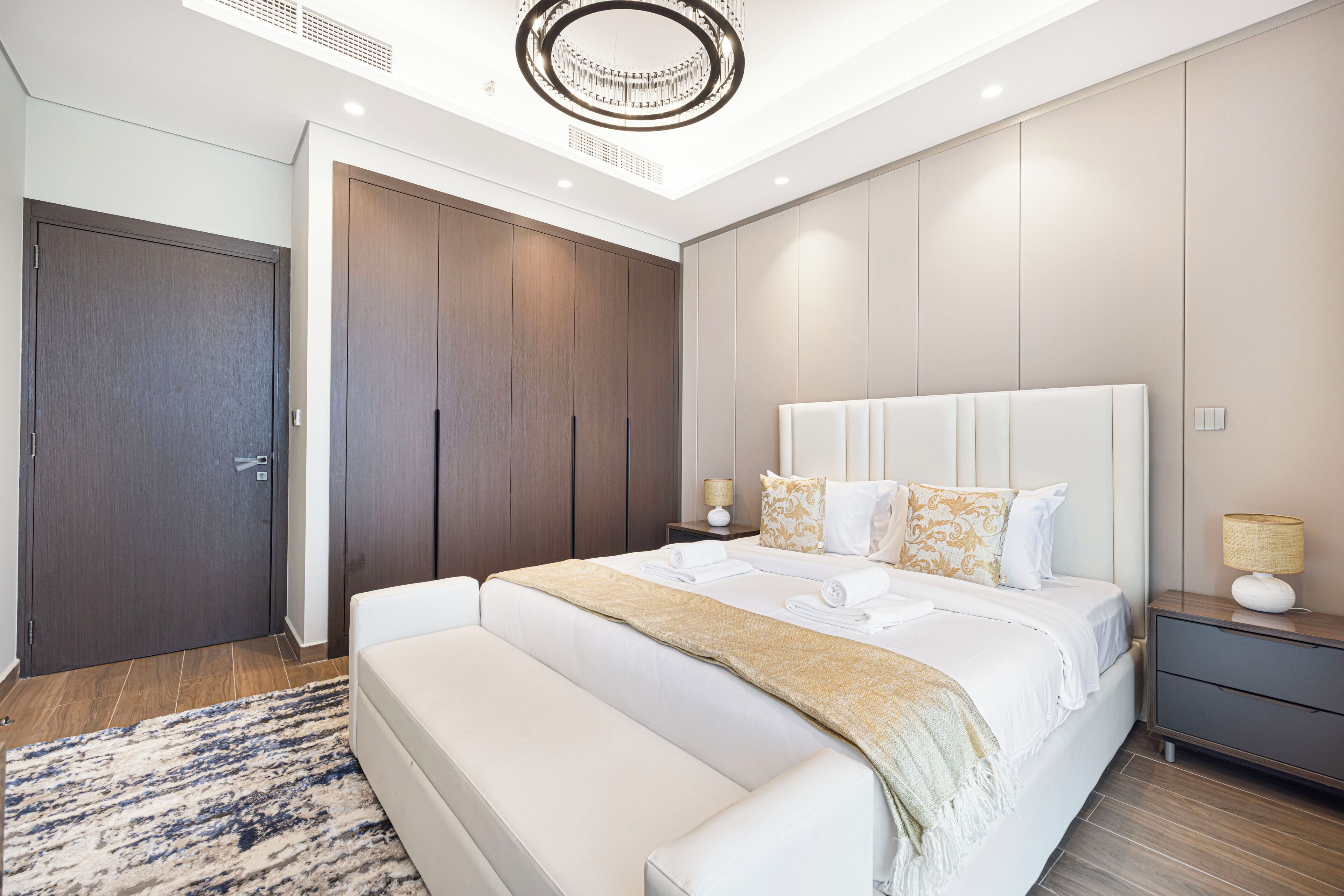 A modern bedroom with a large bed, a bench, a wardrobe, and a nightstand with a lamp.