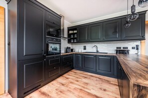 Une cuisine moderne avec des meubles de couleur sombre, un plan de travail en bois et un four encastré.