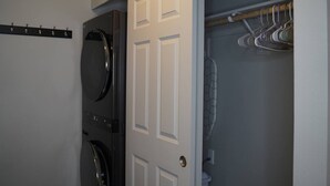 A laundry room with two stacked washers and dryers, a coat rack, and a door leading to a closet.
