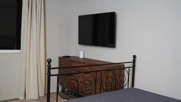 A bedroom with a bed, a dresser, a television mounted on the wall, and a window with curtains.