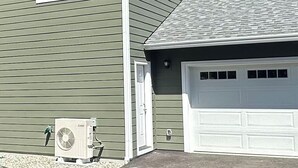 A house with a garage door, a small air conditioning unit, and a door.