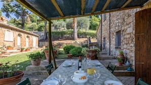 An outdoor dining area with a table set for two, surrounded by potted plants and a stone wall.