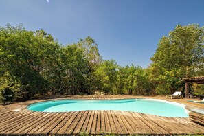 En træterrasse omgiver en swimmingpool med liggestole og en pergola.
