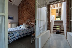 A bedroom with a bed, a window with curtains, a brick wall, and a wooden staircase. - Beautiful private villa for 10 people with sauna, private pool, WIFI and veranda (Agazzano)