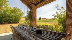 Una mesa de madera al aire libre con sillas, rodeada por un muro de ladrillo y vistas a un campo verde.