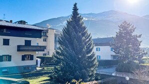 A residential area with houses, a large evergreen tree, and mountains in the background. - Monte Confinale Garden View by Interhome (Bormio)